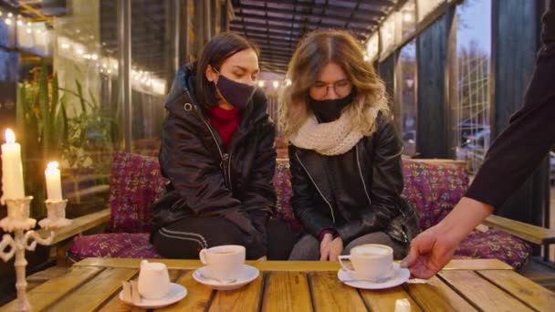 Två glada kvinnor tillbringar tid tillsammans i ett café, restaurang, bär skyddsmasker. karantänsperiod. romantisk kväll med levande ljus, ljus atmosfär, livsstil. Dricka kaffe tillsammans.. — Stockvideo