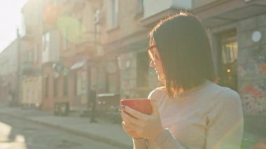 Rahatlamış, gülümseyen, kırmızı kahve fincanı olan, güneşli bir günün tadını çıkaran bir kadın..