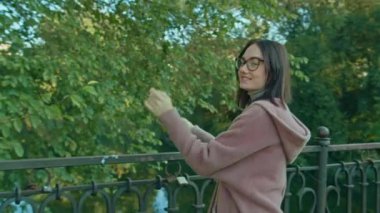 Gözlüklü genç mutlu kadın şehir parkında köprü boyunca yürüyor. sonbahar yaz dönemi.