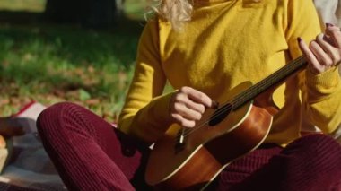 İki mutlu genç kadın şehir parkında harika vakit geçiriyor, bir kız gitar çalıyor, ikincisi ise müziğin ve ağaçların gürültüsünün tadını çıkarıyor. sonbahar yaz dönemi.