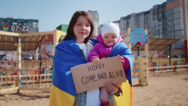 Portret van een vrolijke Oekraïense vrouw met een kind en een Oekraïense vlag. Het meisje wacht op haar man uit de oorlog. Oorlog tussen Rusland en Oekraïne. — Stockvideo
