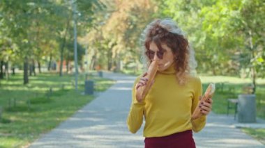 Şehir parkında baget yiyen genç ve mutlu bir kadın. Kızlar birlikte eğleniyor. Gençlik, dinginlik, yaz ya da sonbahar parkı.