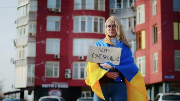 Ukrayna bayrağı ve bir işaret taşıyan neşeli bir Ukraynalı kadının portresi. Kız, savaştan kalan kocasını bekliyor. Rusya ile Ukrayna arasındaki savaş. — Stok video