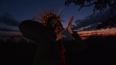 Cadılar Bayramı kostümü içinde mutlu genç bir kadın gün batımında doğada dans ediyor, mistik görüntüler..