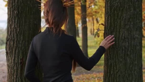 Eine junge Frau mit Santa-Muerte-Make-up in einem schwarzen Totenkleid spaziert bei Sonnenuntergang vor dem Hintergrund von Herbstblättern durch den Wald. Totensonntag oder Halloween-Konzept. — Stockvideo