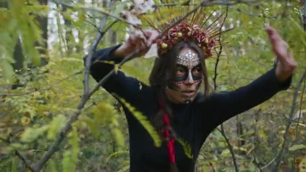一位身穿黑色死亡礼服的年轻女子穿着圣母院的化妆品，落日时分，在森林的秋叶的背景下漫步。死亡日或万圣节的概念. — 图库视频影像