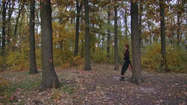 Молодая женщина с макияжем Санта-Муэрте, одетая в черное платье смерти, идет на фоне осенних листьев в лесу на закате. День мертвых, или Хэллоуин. — стоковое видео