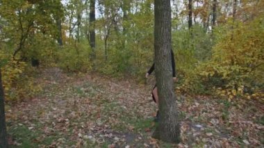 Santa Muerte makyajlı, siyah bir ölüm elbisesi giymiş genç bir kadın günbatımında ormanda sonbahar yapraklarının arka planına doğru yürüyor. Ölüler Günü veya Cadılar Bayramı konsepti.