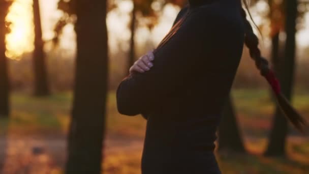 Eine junge Frau mit Santa-Muerte-Make-up in einem schwarzen Totenkleid spaziert bei Sonnenuntergang vor dem Hintergrund von Herbstblättern durch den Wald. Totensonntag oder Halloween-Konzept. — Stockvideo