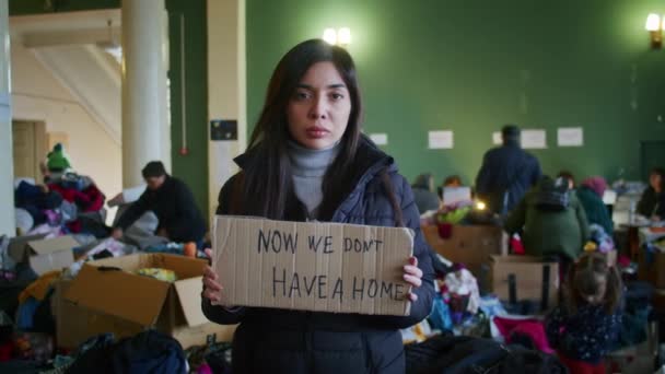 Un retrato de una mujer armenia triste en el gran salón del centro de asistencia a refugiados entre un gran número de ropa y refugiados. Guerra entre Rusia y Ucrania. — Vídeos de Stock