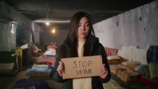 Portrait of a sad Armenian woman, in a large bomb shelter, holding a sign. War between Russia and Ukraine. — Stock Video
