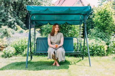 Yazın genç bir kız sıcak çay içer, salıncakta oturur, bahçesinde, çay en iyi sıcakta yardımcı olur, Prores422