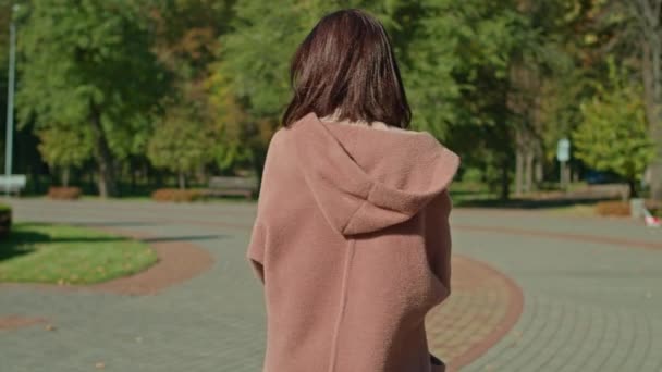 Eine junge, fröhliche Frau mit Brille geht durch den Park. Herbstliche Sommerzeit. — Stockvideo