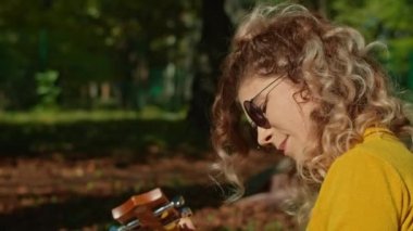 İki mutlu genç kadın şehir parkında harika vakit geçiriyor, bir kız gitar çalıyor, ikincisi ise müziğin ve ağaçların gürültüsünün tadını çıkarıyor. sonbahar yaz dönemi.