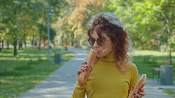 Een jonge vrolijke vrouw die stokbrood eet in het stadspark. Veel plezier samen. jeugd, rust, zomer of herfst park. — Stockvideo