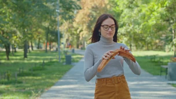 Een jonge vrolijke vrouw die stokbrood eet in het stadspark. Veel plezier samen. jeugd, rust, zomer of herfst park. — Stockvideo