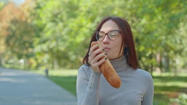 Jovem mulher feliz comendo baguete no parque da cidade. As raparigas divertem-se juntas. juventude, serenidade, verão ou outono parque. — Vídeo de Stock