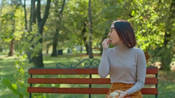 若い幸せな女性はシティパークでバゲットを食べる。女の子は一緒に楽しんでる。若者や静けさ夏や秋の公園. — ストック動画