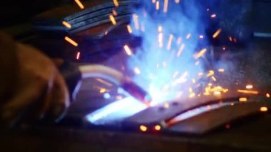 Kapalı çekimde, bir adam yaydan çıkan çelik yelek için plaka kaynatıyor. Ev yapımı zırh plakası. Fabrika işçisi metali kaynaklıyor. Adam kaynak yapıyor. Kaynak makinesi kullanarak argon veya elektrot ile kaynak yapmak. Kıvılcım ve