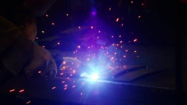 Kapalı çekimde, bir adam yaydan çıkan çelik yelek için plaka kaynatıyor. Ev yapımı zırh plakası. Fabrika işçisi metali kaynaklıyor. Adam kaynak yapıyor. Kaynak makinesi kullanarak argon veya elektrot ile kaynak yapmak. Kıvılcım ve