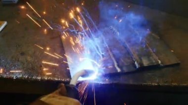 Kapalı çekimde, bir adam yaydan çıkan çelik yelek için plaka kaynatıyor. Ev yapımı zırh plakası. Fabrika işçisi metali kaynaklıyor. Adam kaynak yapıyor. Kaynak makinesi kullanarak argon veya elektrot ile kaynak yapmak. Kıvılcım ve