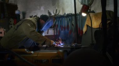 Bir adam yaydan çıkan vücut zırhı için plaka kaynatıyor. Ev yapımı zırh plakası. Fabrika işçisi metali kaynaklıyor. Adam kaynak yapıyor. Kaynak makinesi kullanarak argon veya elektrot ile kaynak yapmak. Kıvılcımlar ve parıltılar uçuşuyor