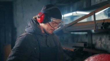 Yorgun bir fabrika işçisinin portresi. Metal yapıları kesmek, kesme makinesi kullanarak profesyonel işçiler tarafından ev yapımı zırh kalıpları yapmak. Çelik metal için pürüzsüz ekipman ile kesme işi