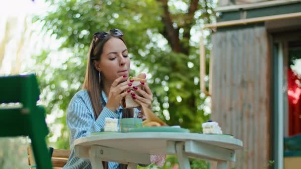 Jovem mulher feliz comer um sanduíche em um café de verão. — Vídeo de Stock