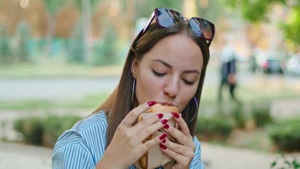 Νεαρή ευτυχισμένη γυναίκα τρώει ένα σάντουιτς σε ένα καλοκαιρινό καφέ. — Αρχείο Βίντεο