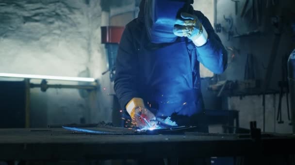 Tiro de um trabalhador cansado em uma fábrica. soldagem de estrutura de aço, fazendo placa de armadura caseira por trabalhador profissional usando máquina de solda, soldagem de ferro, faíscas na indústria pesada fábrica dentro de casa. conflito — Vídeo de Stock