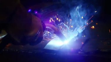 Kapalı çekimde, bir adam yaydan çıkan çelik yelek için plaka kaynatıyor. Ev yapımı zırh plakası. Fabrika işçisi metali kaynaklıyor. Adam kaynak yapıyor. Kaynak makinesi kullanarak argon veya elektrot ile kaynak yapmak. Kıvılcım ve