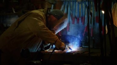 Bir adam yaydan çıkan vücut zırhı için plaka kaynatıyor. Ev yapımı zırh plakası. Fabrika işçisi metali kaynaklıyor. Adam kaynak yapıyor. Kaynak makinesi kullanarak argon veya elektrot ile kaynak yapmak. Kıvılcımlar ve parıltılar uçuşuyor