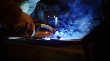 Kapalı çekimde, bir adam yaydan çıkan çelik yelek için plaka kaynatıyor. Ev yapımı zırh plakası. Fabrika işçisi metali kaynaklıyor. Adam kaynak yapıyor. Kaynak makinesi kullanarak argon veya elektrot ile kaynak yapmak. Kıvılcım ve