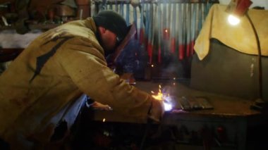 Bir adam yaydan çıkan vücut zırhı için plaka kaynatıyor. Ev yapımı zırh plakası. Fabrika işçisi metali kaynaklıyor. Adam kaynak yapıyor. Kaynak makinesi kullanarak argon veya elektrot ile kaynak yapmak. Kıvılcımlar ve parıltılar uçuşuyor
