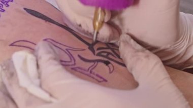 Profesyonel bir dövme sanatçısı, yetişkin bir adamın kolunda dövme yapar. Dövmede Rus savaş gemisine gidin yazıyor. Ukrayna ve Rusya arasındaki çatışma. Savaş 2022.