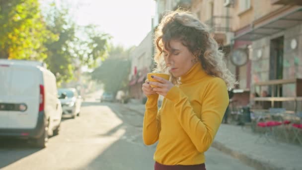 Relaxed smiling satisfied woman with red cup of coffee standing on the street end enjoying a sunny day. — Stock Video