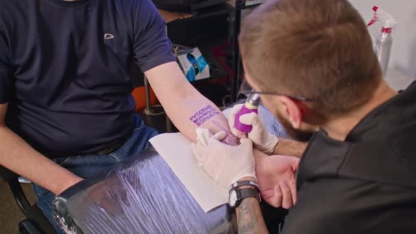 Egy profi tetováló művész egy felnőtt férfi karjára tetovál. Az ukrán úgy döntött, hogy tetováltat - megy orosz hadihajó. konfliktus Ukrajna és Oroszország között. háború 2022. — Stock videók