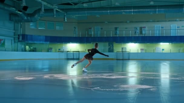 Jonge vrouw kunstschaatser is bezig met kunstschaatsen op ijs. Ze maakt verschillende bewegingen en pirouettes. opleiding choreografie op de ijsbaan voor de start van de wedstrijd. Technologieconcept — Stockvideo