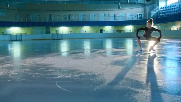 Mujer joven patinador artístico se dedica a patinar sobre hielo. hace diferentes movimientos y piruetas. coreografía de entrenamiento en la pista antes del inicio de la competición. Concepto tecnológico — Vídeos de Stock