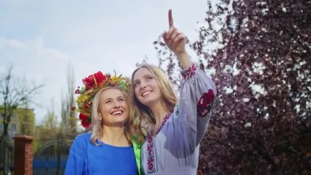 머리에 화관을 쓰고 행복해 하는 두 여인 이 분홍빛 사쿠라 꽃이 피는 배경을 보고 기뻐 한다. 주말에는 해가질 때 미소를 띠고 산책을 한다. 여자와 봄. — 비디오