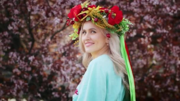 A happy woman in a wreath on her head rejoices against the backdrop of blooming pink sakura flowers. Weekend stroll with a smile at sunset. woman and spring. — Stock Video