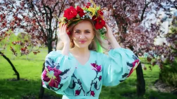 A happy woman in a wreath on her head rejoices against the backdrop of blooming pink sakura flowers. Weekend stroll with a smile at sunset. woman and spring. — стоковое видео