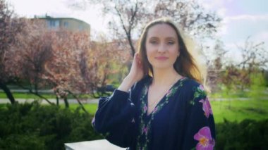 Mutlu kadın çiçek açan pembe sakura çiçeklerinin arka planına seviniyor. Hafta sonu yürüyüşü, gün batımında bir gülümsemeyle. Kadın ve bahar.