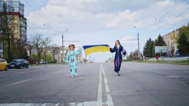 Zwei glückliche Frauen jubeln und gehen die Straße entlang mit der Fahne der Ukraine. Wochenendspaziergang mit einem Lächeln bei Sonnenuntergang. Frau und Frühling. — Stockvideo