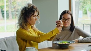 two young happy women enjoy delicious salad of chicken, tomato and croutons, eat it with a fork in a beautiful cool place in hot summer.