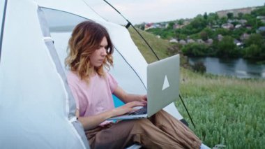 Genç bir kadın, dağ tepelerinde, dizüstü bilgisayarla iletişim kurmaktan mutlu olur, tatilde çalışır. Doğadaki bir kişinin geri kalanı, dağlarda. uzak çalışma