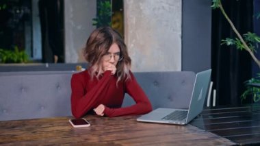 sad tired young woman sits with phone and computer at the table. business time. rest and work
