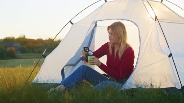一个年轻的女人在日落时高兴地在山上搭起一个帐篷 在远足之后休息 喝热茶的女人 一个人在自然界中的休息 在山里 — 图库视频影像