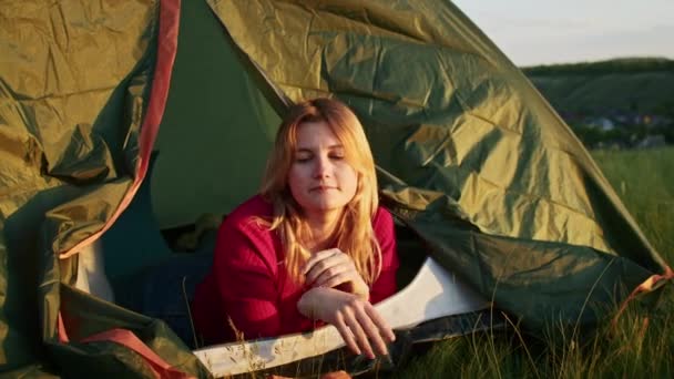 若い女性はハイキングの後の休息のために喜んで日没の間に山の丘の上のテントを離れる 残りの1人は山の中で — ストック動画