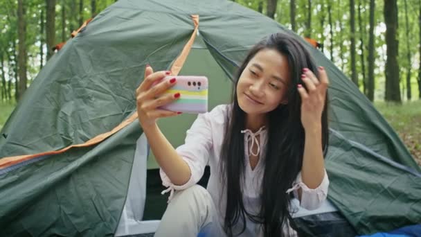 아시아인 여자는 공원에서 텐트를 치면서 휴가를 즐기고 비디오 통화를 통화를 — 비디오